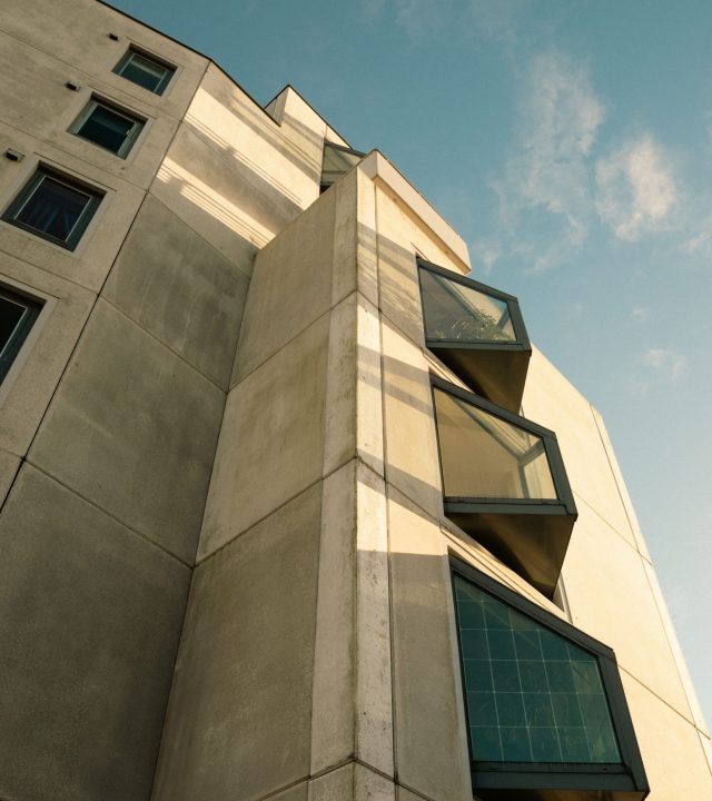 A low-angle view of a modern concrete building with large windows against a clear sky.